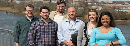 Six people standing on a bridge smiling at the camera.