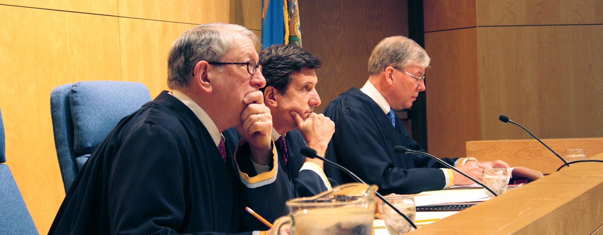 3 men from the Delaware Supreme Court leaning forward over a desk.